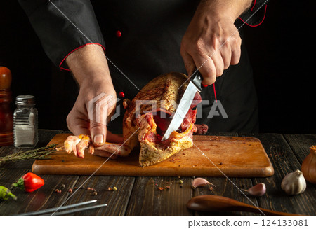 Cutting a raw duck carcass with a knife in the hands of a skilled butcher. Cooking a meat dish from the bird for lunch on the kitchen table with aromatic spices. 124133081