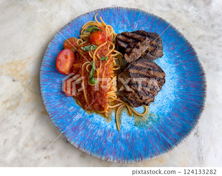 Juicy grilled steak with spaghetti in rich tomato sauce garnished with fresh basil on a stylish blue plate 124133282