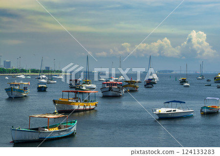 Serene coastal scene with anchored boats on calm waters under a colorful sky at sunset 124133283