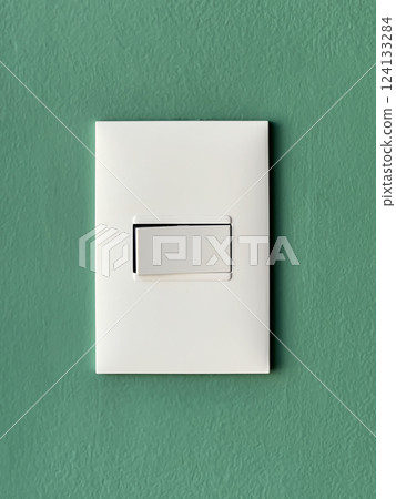 White modern minimalist light switch mounted on a textured green wall in a simple interior design 124133284