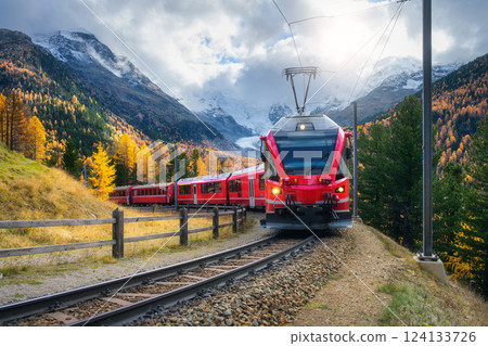 Red modern electric train traveling along a railway in mountains Red modern electric train traveling along a railway in mountains 124133726