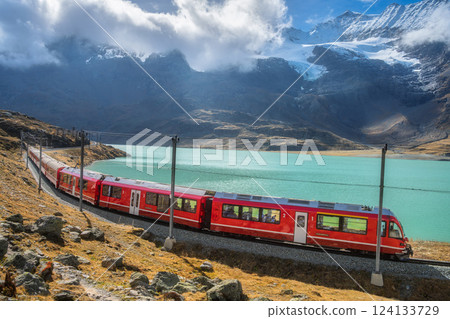 Red train is moving along railway in swiss alps mountain. Autumn 124133729
