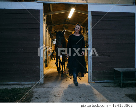 Woman Leading Horse Out of Stable at Evening 124133802
