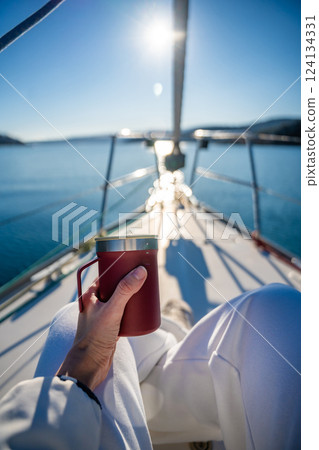 Woman hands holding thermo mug sitting on bow of the yacht during sailing in the morning in winter time in Adriatic sea, relaxation in yachting time Woman hands holding thermo mug sitting on bow of the yacht during sailing in the morning in winter time in Adriatic sea, relaxation in yachting time 124134331