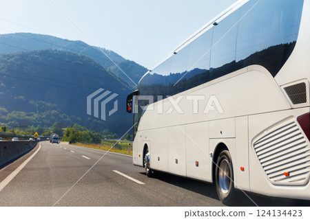 Scenic back view big luxury white comfortable tourist bus driving through highway on bright sunny day mountain landscape background. Travel and coach tourism concept. Trip and journey by vehicle Scenic back view big luxury white comfortable tourist bus driving through highway on bright sunny day mountain landscape background. Travel and coach tourism concept. Trip and journey by vehicle 124134423