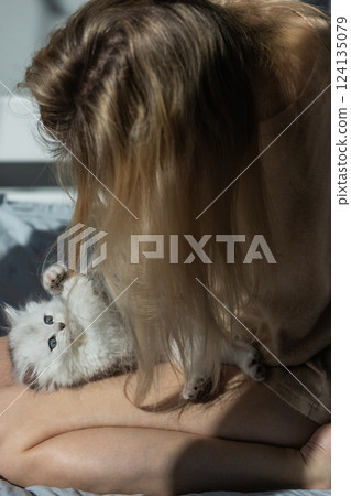 A Cozy Moment: A Woman Playfully Interacting with Her Adorable White Kitten in a Sunlit Room, Capturing the Bond of Love and Companionship on a Relaxed Morning A Cozy Moment: A Woman Playfully Interacting with Her Adorable White Kitten in a Sunlit Room, Capturing the Bond of Love and Companionship on a Relaxed Morning 124135079