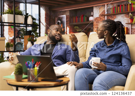 Happy people relaxing together on their comfortable sofa enjoying tea and casual conversation, laughing during leisure time. Affectionate bond and warmth make for a heartwarming lifestyle. 124136437