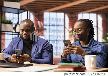 African american couple checking their online correspondence on phones, sending emails before starting daily freelancing tasks. Young adults living and working remotely together. African american couple checking their online correspondence on phones, sending emails before starting daily freelancing tasks. Young adults living and working remotely together. 124136451