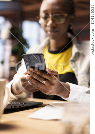 Person reading messages on mobile phone in home office, having conversation with mates, close up shot. Woman in apartment reading SMS on smartphone device, chatting with friends 124136535