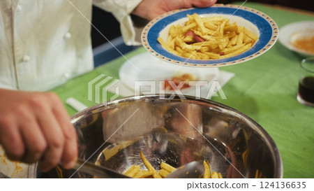 Chef Is Portioning French Fries and Sausages onto Plates in an Italian Cooking 124136635