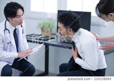 圖片中,一名醫生正在檢查一名身體不適的辦公室職員,他因過度勞累而胸痛,看起來好像要嘔吐 圖片中,一名醫生正在檢查一名身體不適的辦公室職員,他因過度勞累而胸痛,看起來好像要嘔吐 124138084