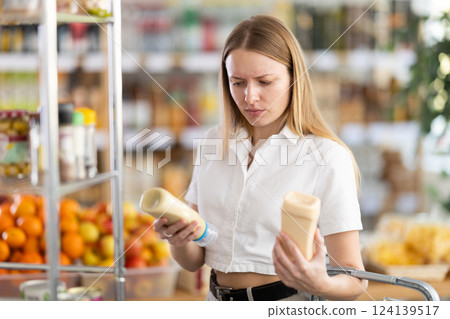 Young woman choosing mayonnaise in grocery store Young woman choosing mayonnaise in grocery store 124139517