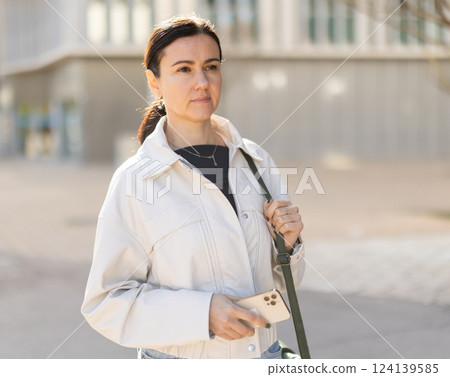 Portrait of brunette woman with mobile phone on street of european city 124139585