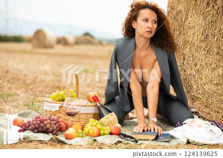 Topless girl in trousers is sitting with glass of wine and book near haystack Topless girl in trousers is sitting with glass of wine and book near haystack 124139625