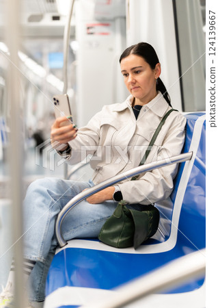 Woman in metro carriage points phone camera at an information board Woman in metro carriage points phone camera at an information board 124139667
