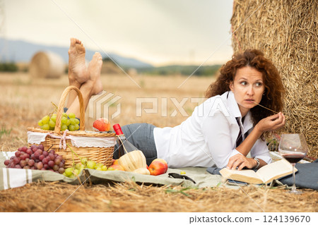 Businesswoman finding solitude by haystack with wine and book 124139670