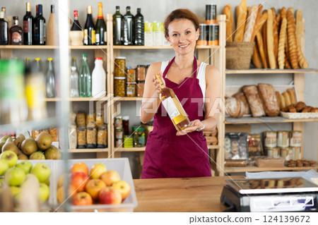 Adult woman seller offers wine in grocery store Adult woman seller offers wine in grocery store 124139672