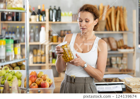 Female shopper carefully choosing jar of canned olives in grocery supermarket Female shopper carefully choosing jar of canned olives in grocery supermarket 124139674
