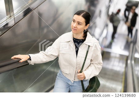 Woman coming out of metro station, moving up on escalator 124139680