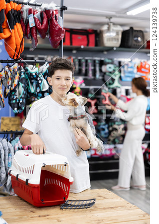 Smiling teenager standing with dog carrier and Yorkshire terrier in pet store 124139738