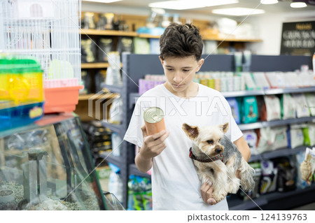 Boy with dog Yorkshire terrier in arms and read composition of product at packaging of dog dry food 124139763