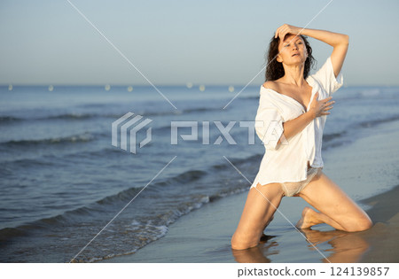 Topless woman in white shirt kneeling on coast Topless woman in white shirt kneeling on coast 124139857