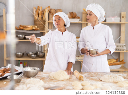 Elderly female baker giving advice to young assistant in kitchen 124139888