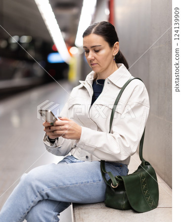 Woman sits on bench at metro station in anticipation of train Woman sits on bench at metro station in anticipation of train 124139909