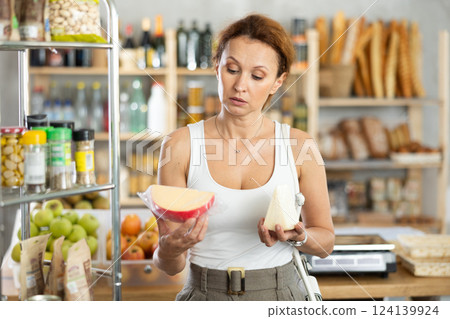 Woman carefully chooses delicious cheese in grocery department of supermarket 124139924