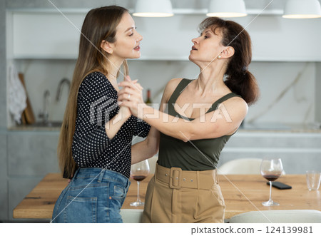 Two joyful middle-aged women dancing together at the kitchen-table with wineglasses 124139981
