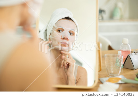 Woman with towel head wrap applying cosmetic face mask Woman with towel head wrap applying cosmetic face mask 124140022