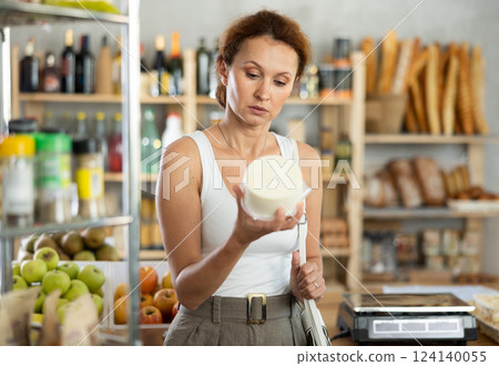 Woman carefully chooses delicious cheese in grocery department of supermarket Woman carefully chooses delicious cheese in grocery department of supermarket 124140055