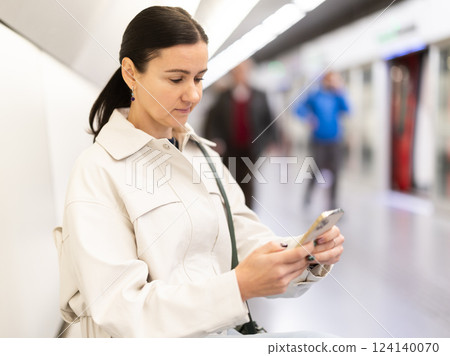 Girl with phone is sitting on metro platform station, scrolling though internet Girl with phone is sitting on metro platform station, scrolling though internet 124140070