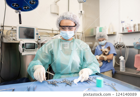Woman veterinarian in full protective gear arranges instrument on desktop, prepares to treat patient 124140089
