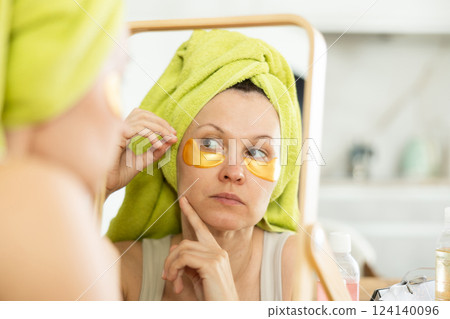 Woman with towel headwrap applying under-eye patches Woman with towel headwrap applying under-eye patches 124140096