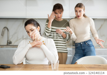 Upset middle-aged woman sitting at the kitchen table with her back to women quarreling to her 124140114