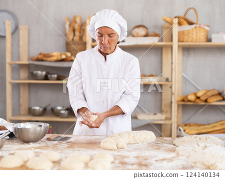 Elderly woman baker molding pieces of dough 124140134