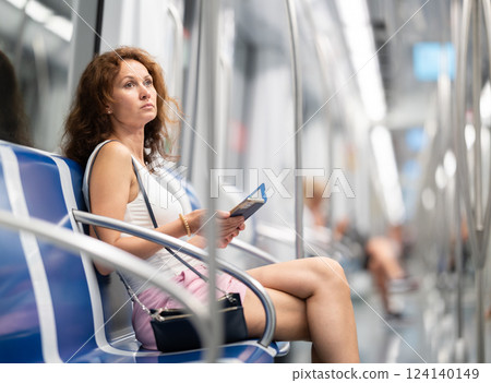 Adult woman sitting in subway car with phone Adult woman sitting in subway car with phone 124140149