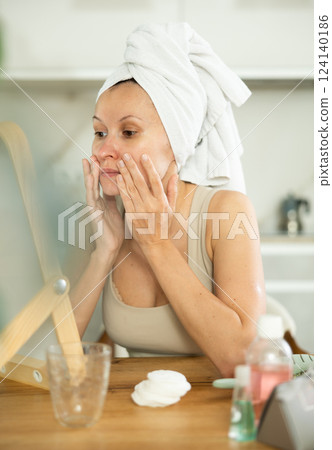 Middle-aged woman examining her facial skin looking in the mirror put on the table 124140186