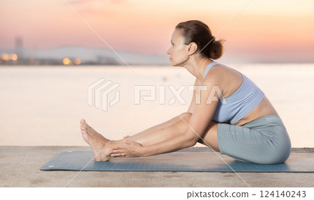 Near sea during sunset, girl performs Pashchimottanasana Near sea during sunset, girl performs Pashchimottanasana 124140243