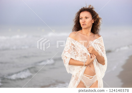 Woman in white negligee stands on coast 124140378