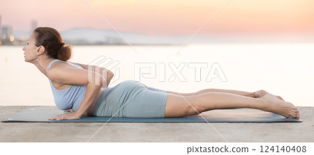 Near sea during sunset, girl performs shalabhasana 124140408