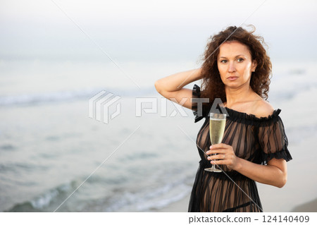Woman in black negligee with champagne on coast 124140409