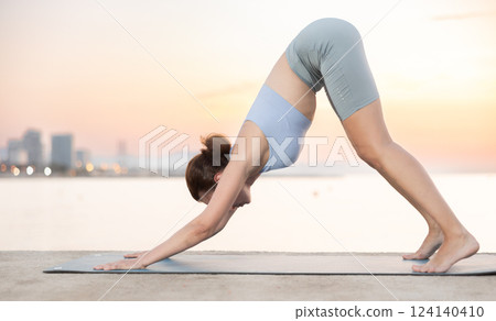 Active woman take care of physical health and practice yoga, perform yoga exercise on beach at sunset 124140410