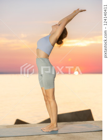 Near sea during sunset, girl performs Tiryaka Tadasana Near sea during sunset, girl performs Tiryaka Tadasana 124140411