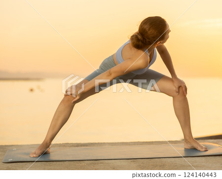 Near sea during sunset, girl performs variations of Himavanasana Near sea during sunset, girl performs variations of Himavanasana 124140443