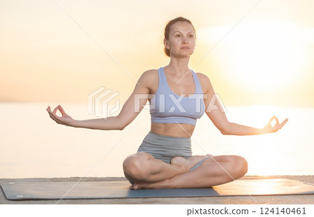 Near sea during sunset, girl performs variations of padmasana Near sea during sunset, girl performs variations of padmasana 124140461