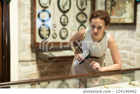 Woman with paper and phone in hands walks around hall of museum, examines showpiece at exhibition Woman with paper and phone in hands walks around hall of museum, examines showpiece at exhibition 124140462