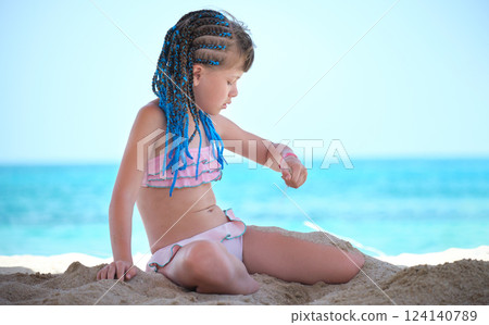Happy child girl in bikini swimsuit playing with sand on seaside beach during summer tropical vacation 124140789