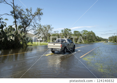 Flooded american street with moving vehicles and surrounded with water houses in Florida residential area. Consequences of hurricane natural disaster 124140832